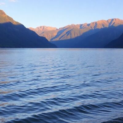 Calm lake at sunrise with mountains and greenery.