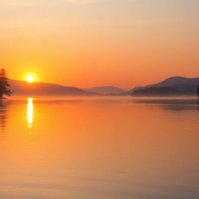 Silhouetted landscape of tranquil lake and trees at sunset.