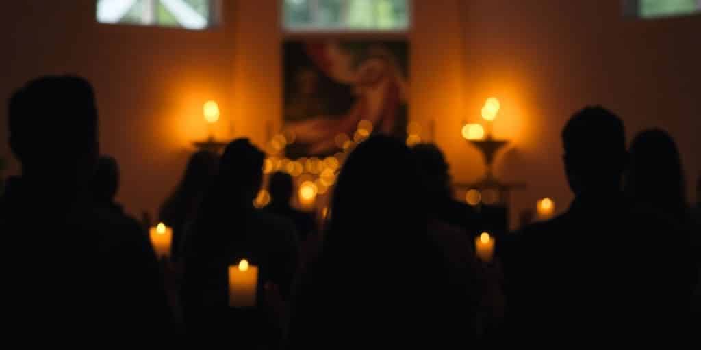 Silhouetted figures in prayer with soft candlelight glow.