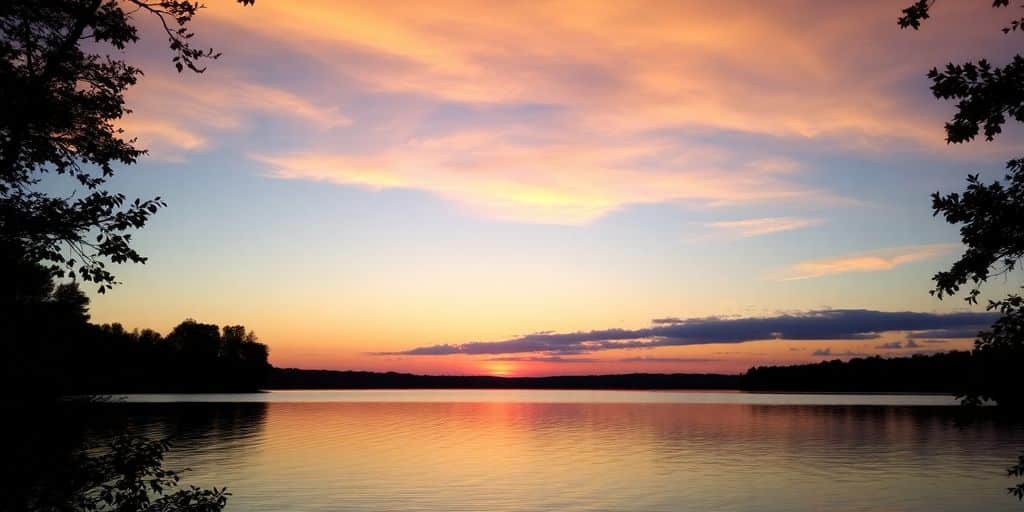 Silhouette of trees by a calm lake at sunset.