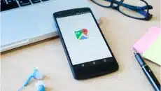 Smartphone displaying Google Maps on a desk with a laptop, glasses, and office supplies, representing local SEO and optimizing Google Business Profiles.